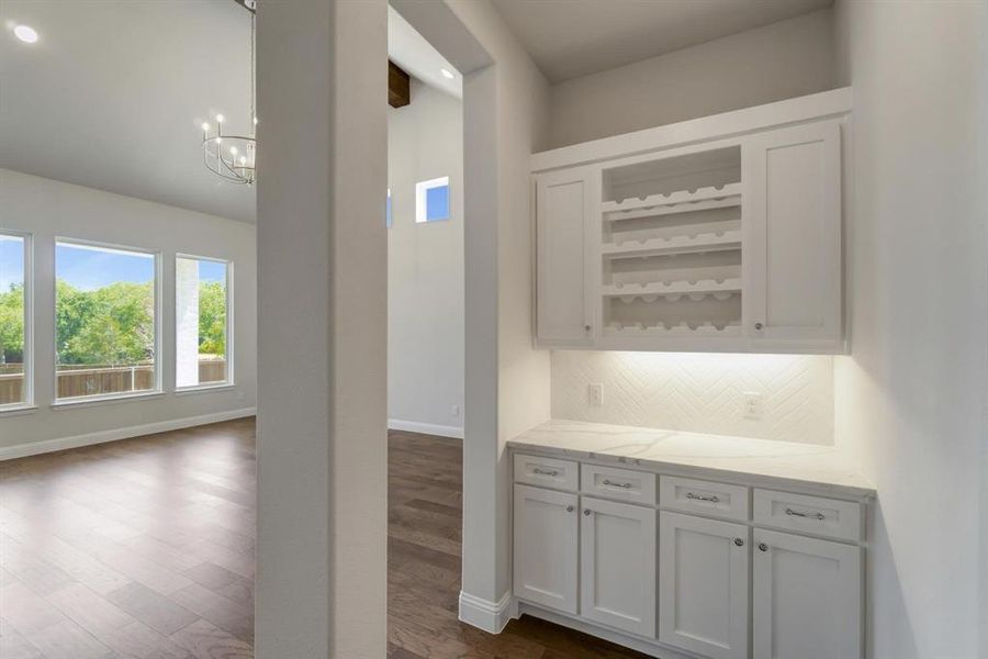 Bar with a chandelier, white cabinets, backsplash, light stone counters, and dark hardwood / wood-style floors