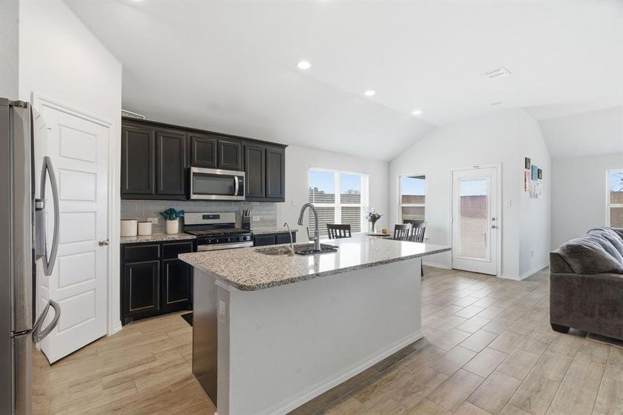 Kitchen featuring appliances with stainless steel finishes, lofted ceiling, light stone counters, open floor plan, and backsplash