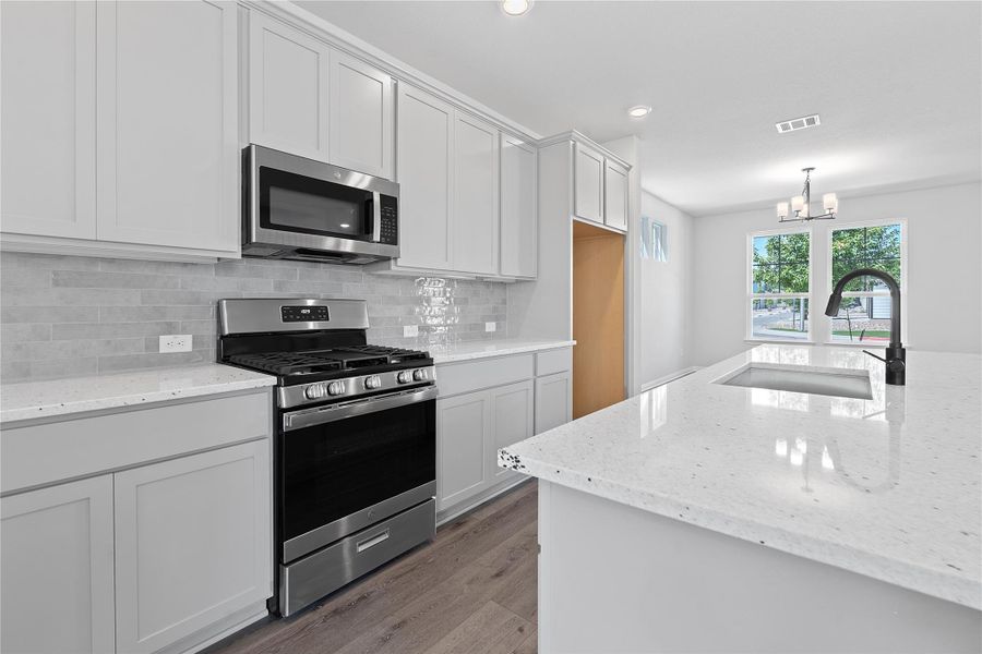 Kitchen featuring appliances with stainless steel finishes, a chandelier, tasteful backsplash, wood finished floors, and light stone counters