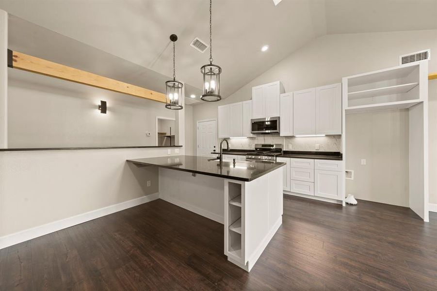Kitchen with open shelves, stainless steel appliances, dark countertops, backsplash, and high vaulted ceiling