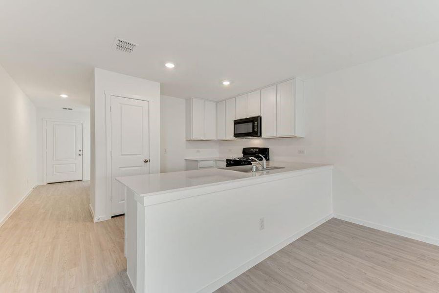 Kitchen featuring light wood finished floors, a peninsula, light countertops, black appliances, and white cabinetry