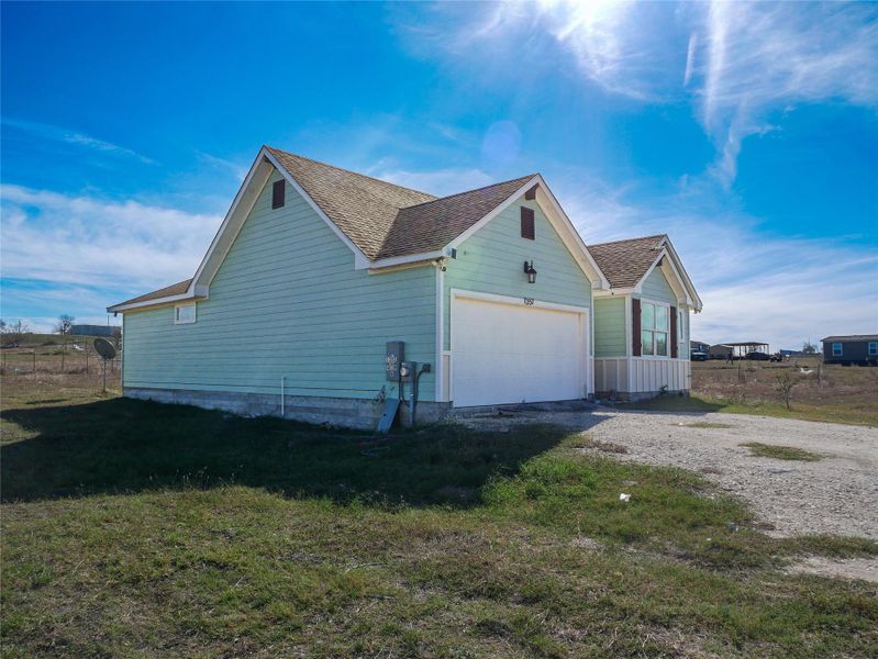 View of home's exterior with driveway, roof with shingles, an attached garage, and a lawn