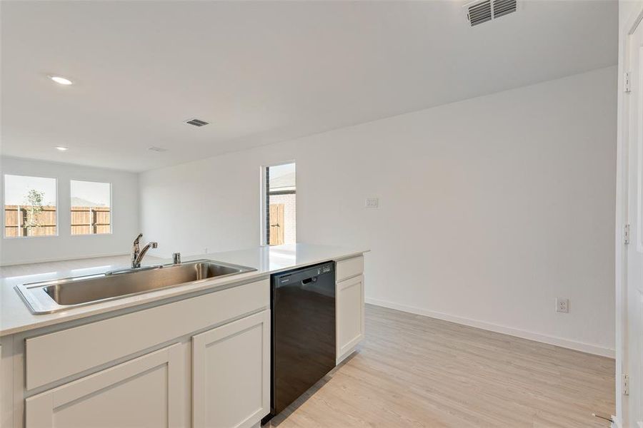 Kitchen with dishwasher, sink, white cabinets, and light wood-type flooring