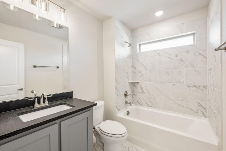 Bathroom with gray vanity, dark countertop, and tub-shower combo with marble-look tile surround Bathroom with gray vanity, dark countertop, and tub-shower combo with marble-look tile surround
