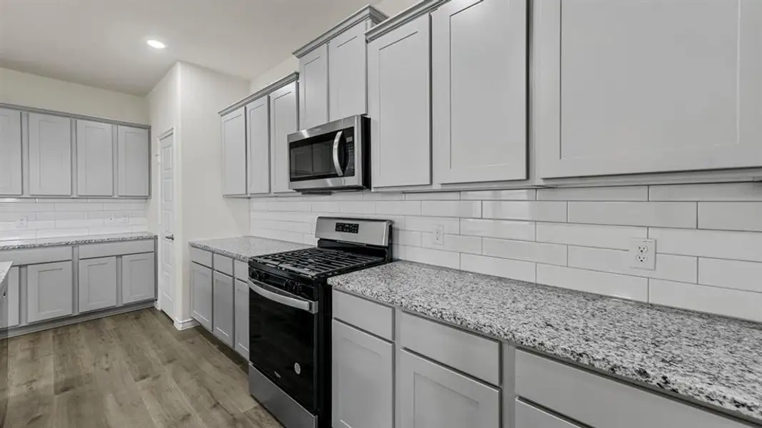 The kitchen features light-colored cabinetry, granite countertops, a subway tile backsplash, stainless steel appliances, and wood-look flooring