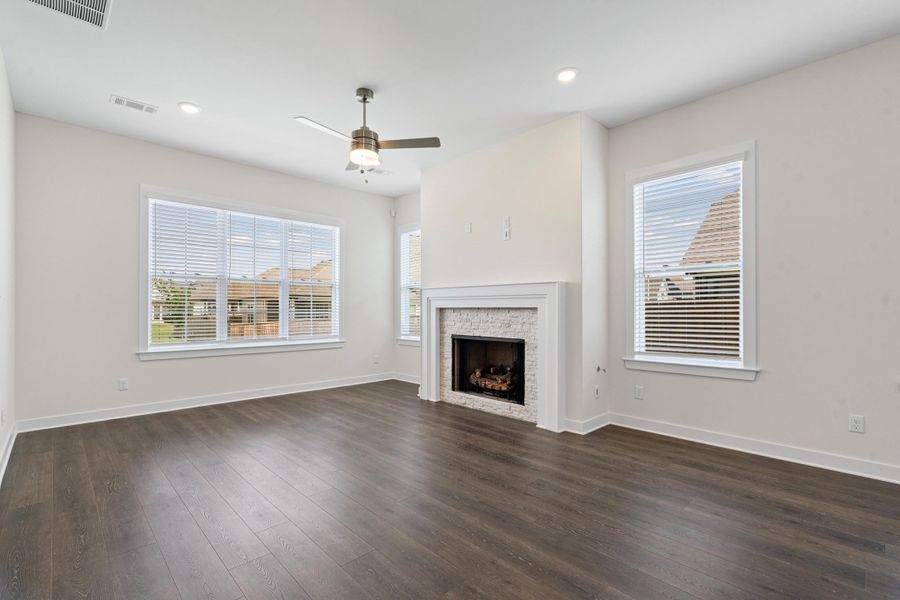 Spacious room featuring wood-finish flooring, a white mantel fireplace with a stacked stone facade, recessed lighting, and a ceiling fan Spacious room featuring wood-finish flooring, a white mantel fireplace with a stacked stone facade, recessed lighting, and a ceiling fan