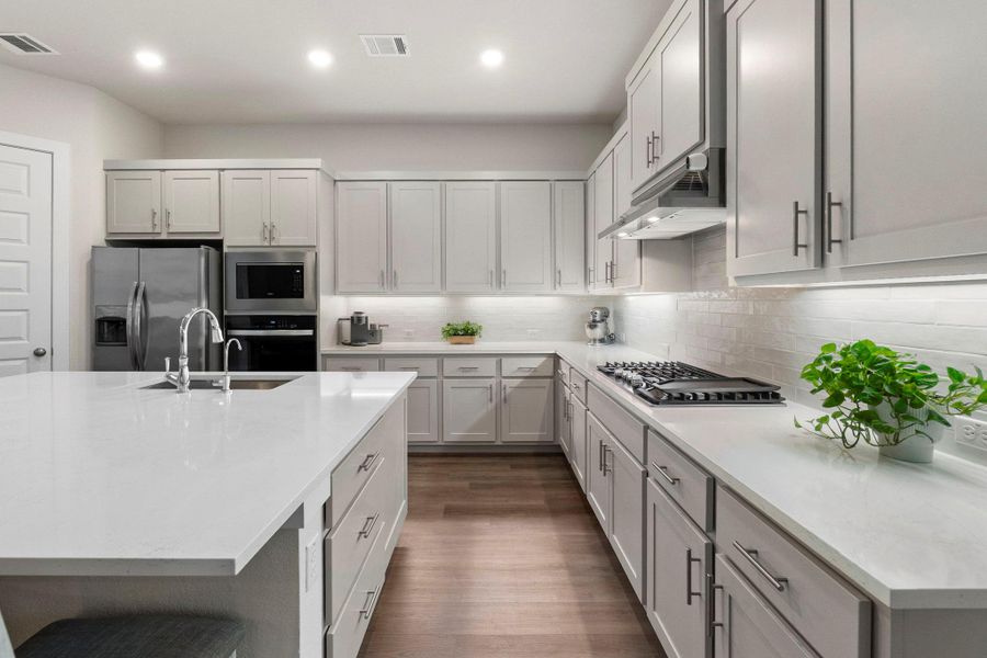 Modern kitchen featuring light gray cabinetry with brushed nickel hardware, white stone countertops, and a white subway tile backsplash