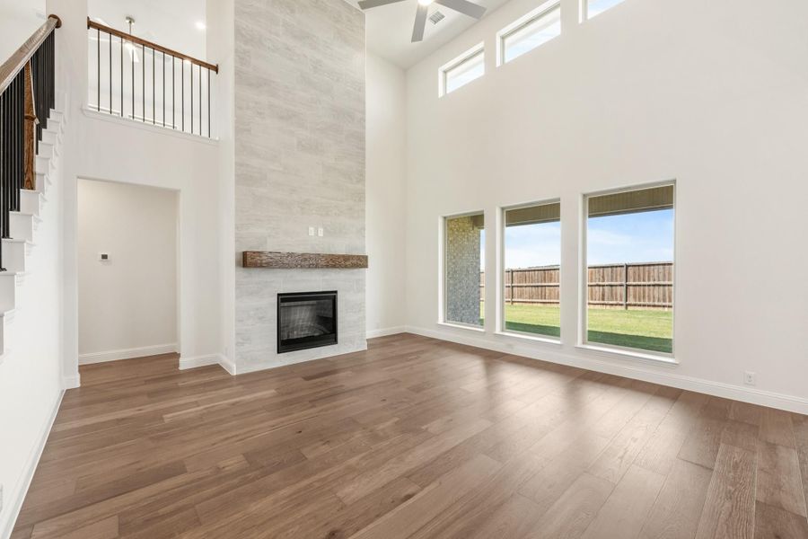Open living room with two-story ceiling, tile fireplace, wood mantel, and hardwood floors Open living room with two-story ceiling, tile fireplace, wood mantel, and hardwood floors