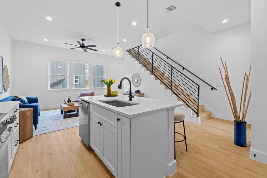 Kitchen featuring open floor plan, a center island with sink, white cabinetry, decorative light fixtures, and light wood-type flooring