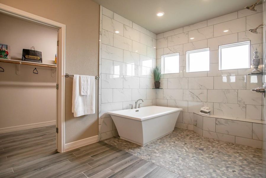 Full bathroom with a freestanding bath, a walk in closet, wood finished floors, tile walls, and recessed lighting Full bathroom with a freestanding bath, a walk in closet, wood finished floors, tile walls, and recessed lighting