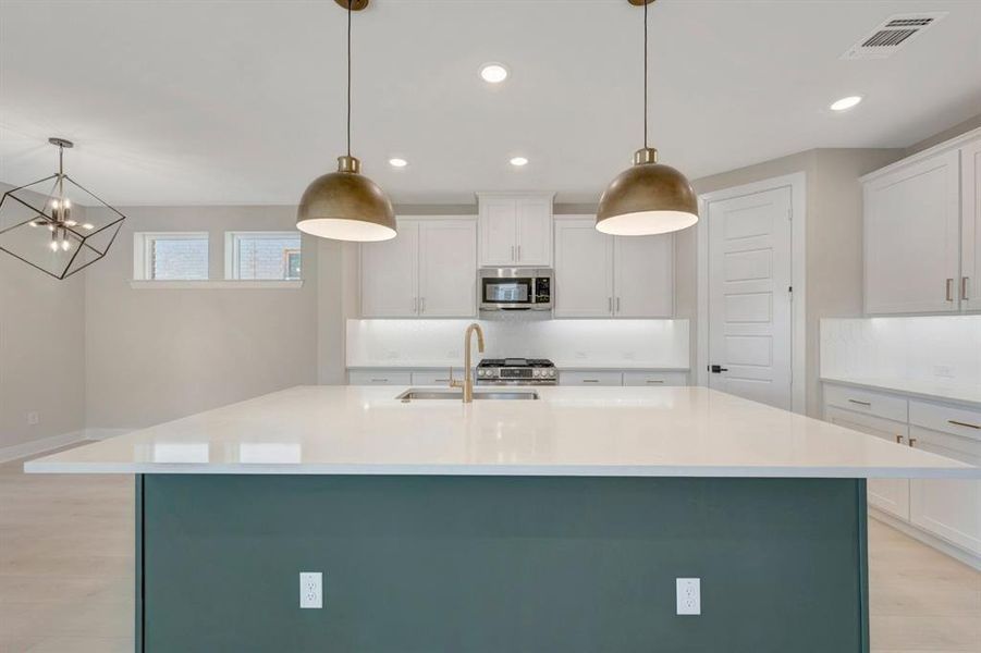 Kitchen featuring two tone cabinets, light wood-style flooring, a center island with sink, stainless steel appliances, and light stone countertops