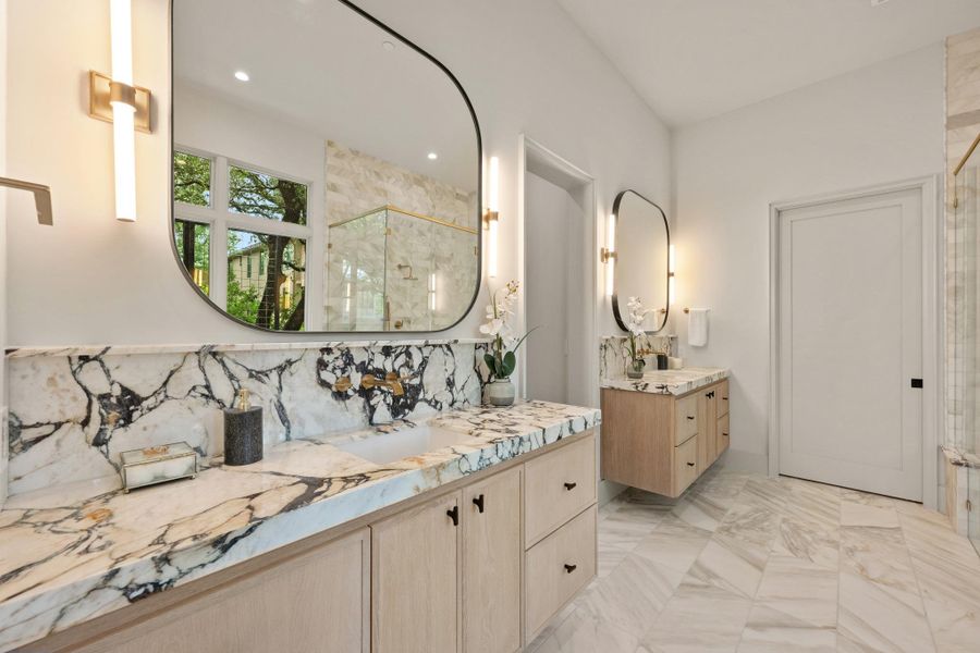 Marble countertops and light wood cabinetry define this elegantly designed primary bathroom. Marble countertops and light wood cabinetry define this elegantly designed primary bathroom.