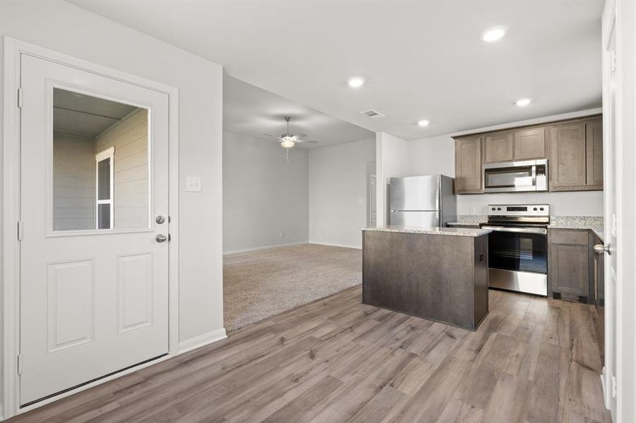 Kitchen with appliances with stainless steel finishes, light stone countertops, a kitchen island, light carpet, and ceiling fan