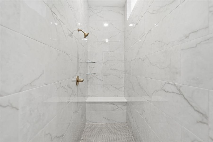 Tiled shower featuring brass fixtures, an integrated bench, two recessed shelves, and a contrasting mosaic tile floor Tiled shower featuring brass fixtures, an integrated bench, two recessed shelves, and a contrasting mosaic tile floor