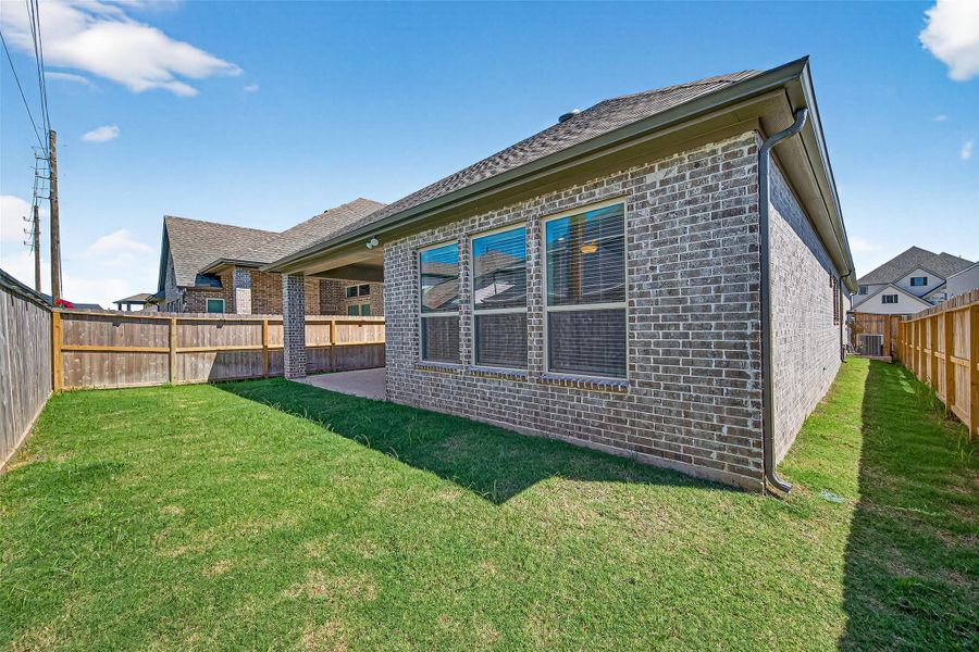 This photo showcases the backyard of a brick house, featuring a neatly maintained lawn, a covered patio, and fenced boundaries for privacy. This photo showcases the backyard of a brick house, featuring a neatly maintained lawn, a covered patio, and fenced boundaries for privacy.
