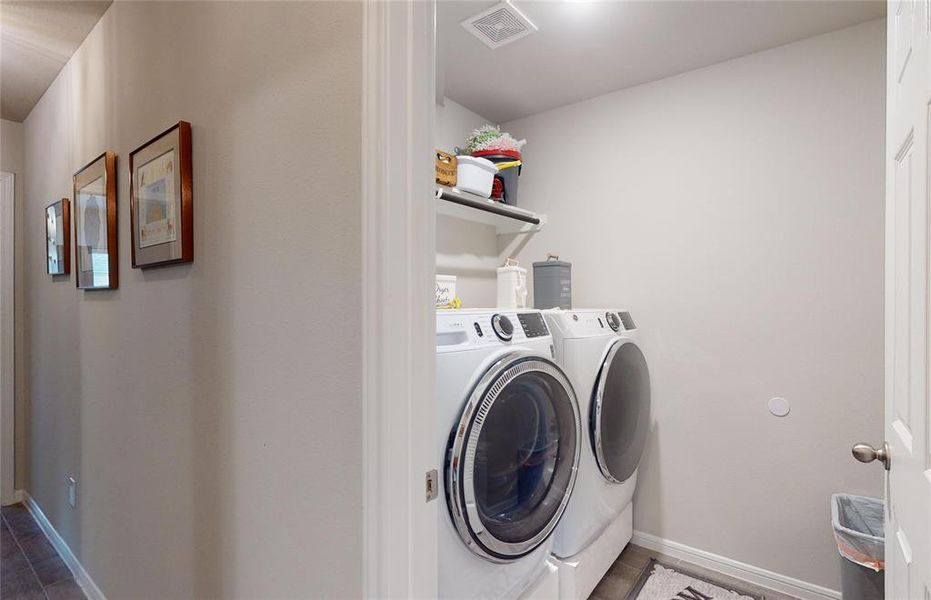 The utility room is compact featuring shelving above for storage of laundry essentials.