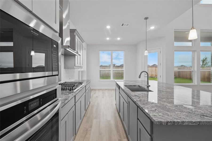 Kitchen featuring stainless steel appliances, a sink, light wood finished floors, wall chimney range hood, and gray cabinets
