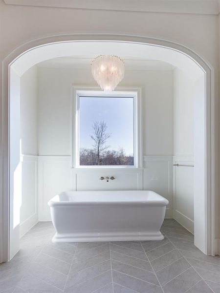 The primary bath features an inset, stand-alone tub surrounded by painted paneling and beautiful patterned floor tile with a gorgeous chandelier!