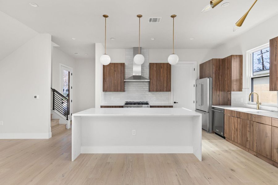 Kitchen featuring visible vents, a sink, stainless steel appliances, wall chimney range hood, and modern cabinets