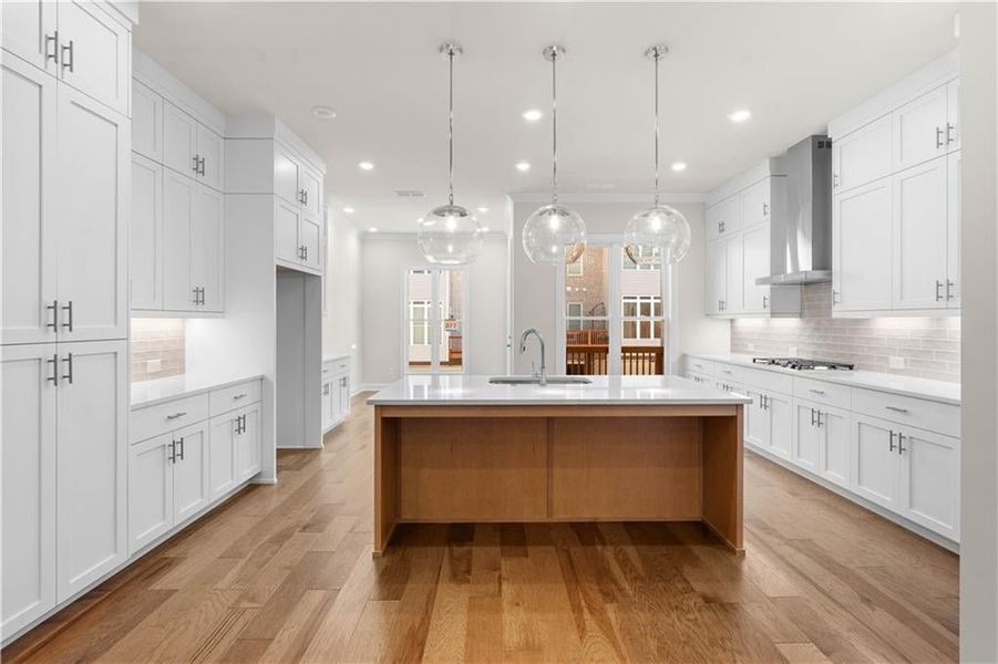 Kitchen with backsplash, white cabinets, hanging light fixtures, light wood finished floors, and light stone countertops