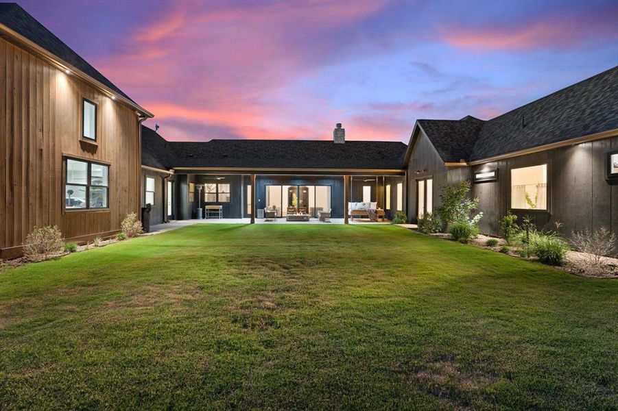 Back house at dusk with a lawn and a patio