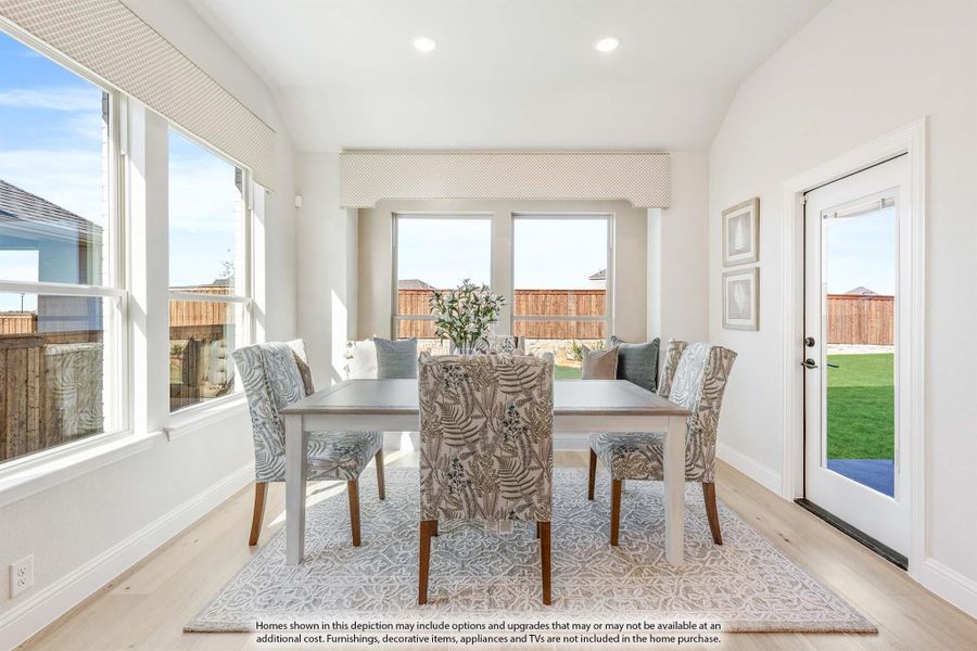 Bright dining room with gray table, patterned chairs, light wood floors, and large windows overlooking a backyard.