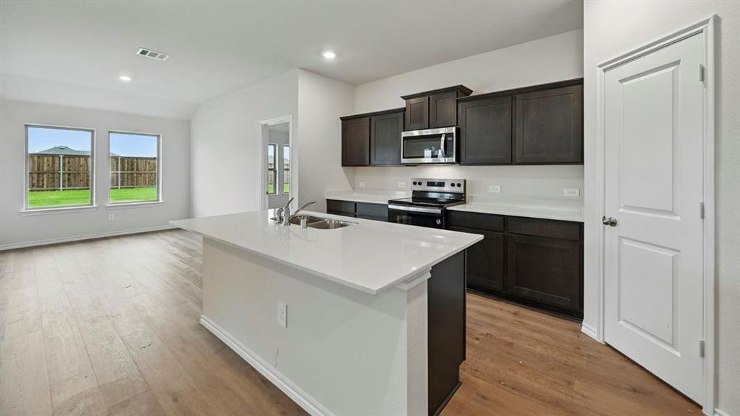 Kitchen with stainless steel appliances, a kitchen island with sink, light wood-style floors, recessed lighting, and light stone counters