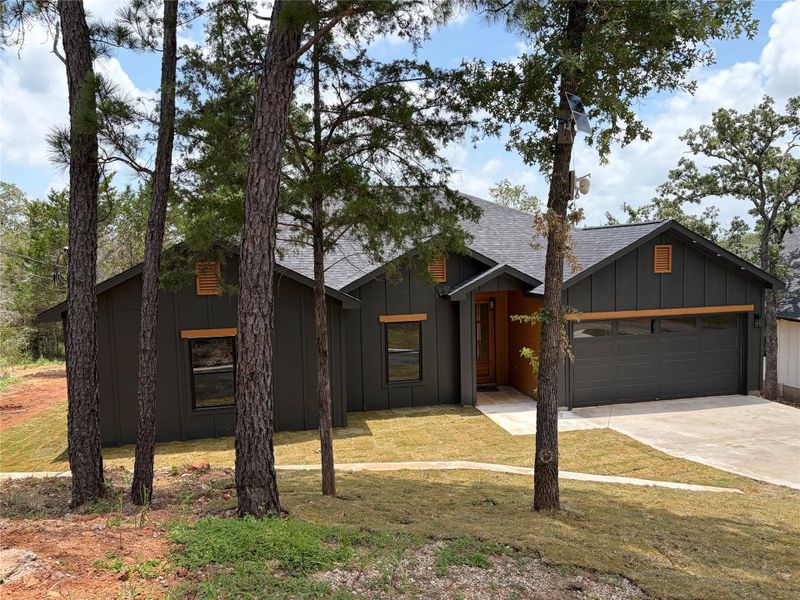Modern dark-clad residence with an attached garage, nestled amongst mature trees and fresh landscaping. Modern dark-clad residence with an attached garage, nestled amongst mature trees and fresh landscaping.