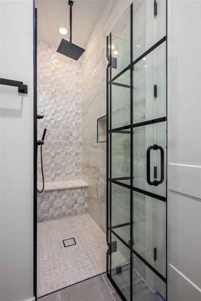 A statement glass-paneled shower enclosure houses a rainfall showerhead, handheld sprayer, and relaxing bench seating