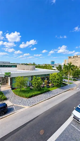 Commercial property featuring a flat roofline, floor-to-ceiling glass paneling, patterned paver walkways, and established green space with mature landscaping Commercial property featuring a flat roofline, floor-to-ceiling glass paneling, patterned paver walkways, and established green space with mature landscaping