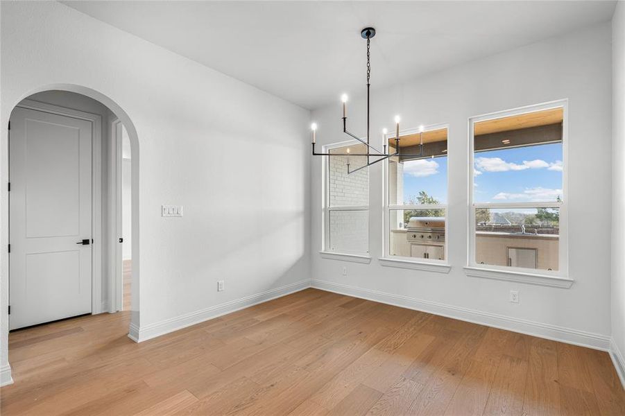 Unfurnished dining area with arched walkways, hanging lights, and light wood-type flooring