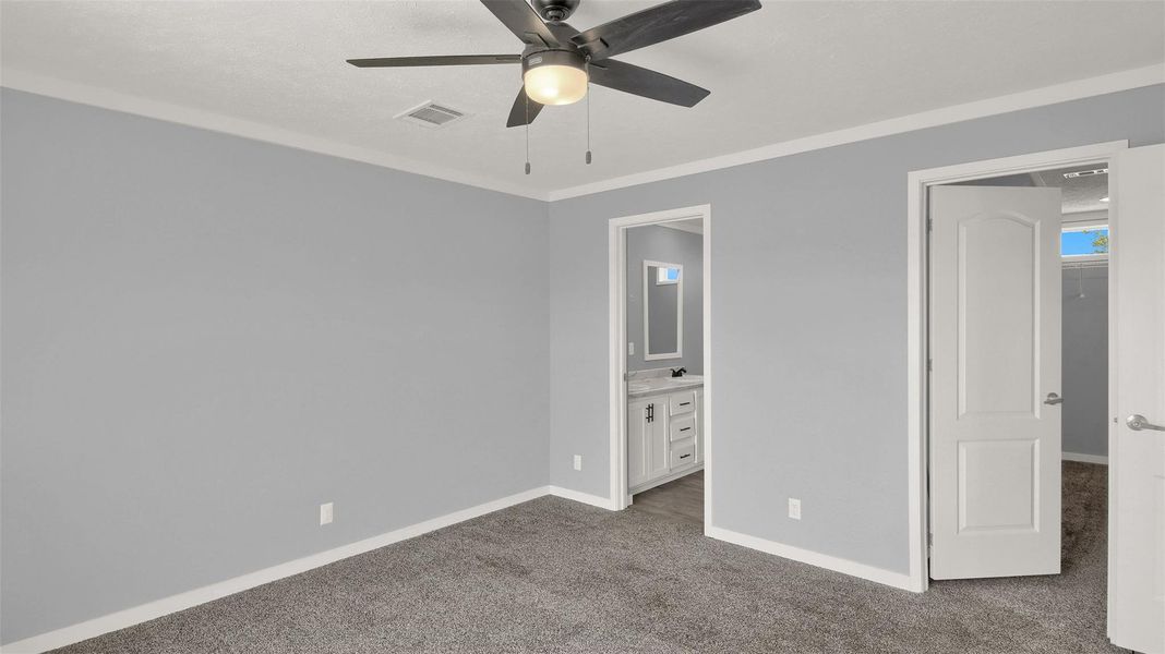 Plush carpeting anchors this spacious bedroom featuring clean crown molding and an attached bath.