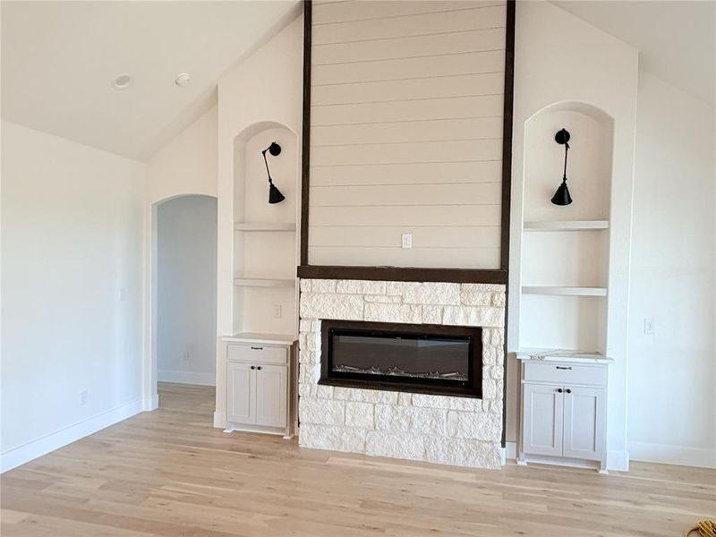 Unfurnished living room with vaulted ceiling, arched walkways, light wood finished floors, a fireplace, and built in features Unfurnished living room with vaulted ceiling, arched walkways, light wood finished floors, a fireplace, and built in features
