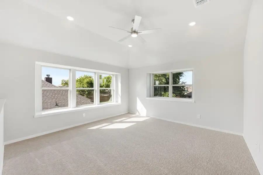 Empty bedroom with vaulted ceiling, ceiling fan, carpet flooring, and two large windows