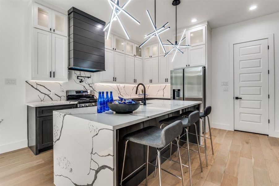 Kitchen with backsplash, white cabinetry, light stone counters, a breakfast bar, and recessed lighting Kitchen with backsplash, white cabinetry, light stone counters, a breakfast bar, and recessed lighting