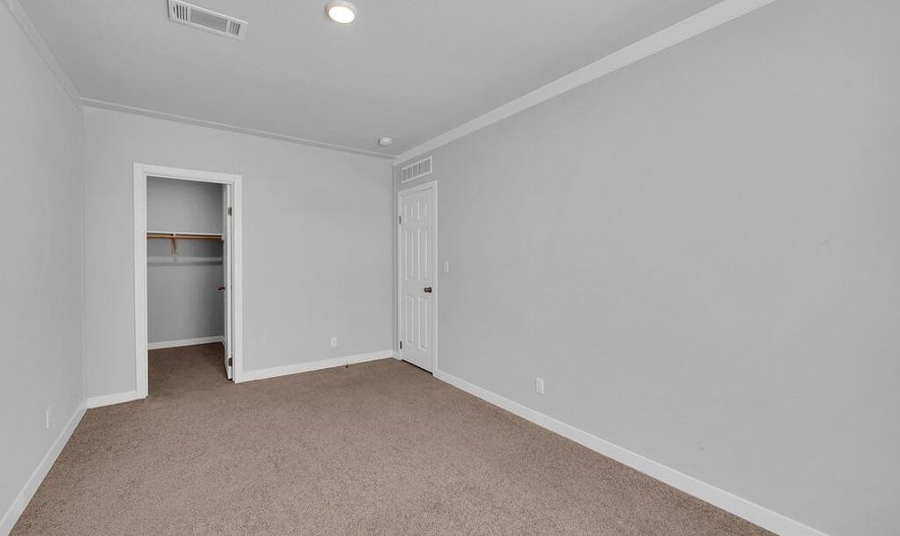 Unfurnished bedroom with a spacious closet, light carpet, crown molding, and recessed lighting Unfurnished bedroom with a spacious closet, light carpet, crown molding, and recessed lighting