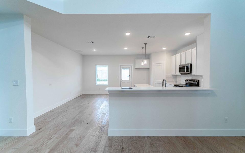 Kitchen with white cabinets, a peninsula, stainless steel microwave, decorative backsplash, and light wood-style flooring Kitchen with white cabinets, a peninsula, stainless steel microwave, decorative backsplash, and light wood-style flooring