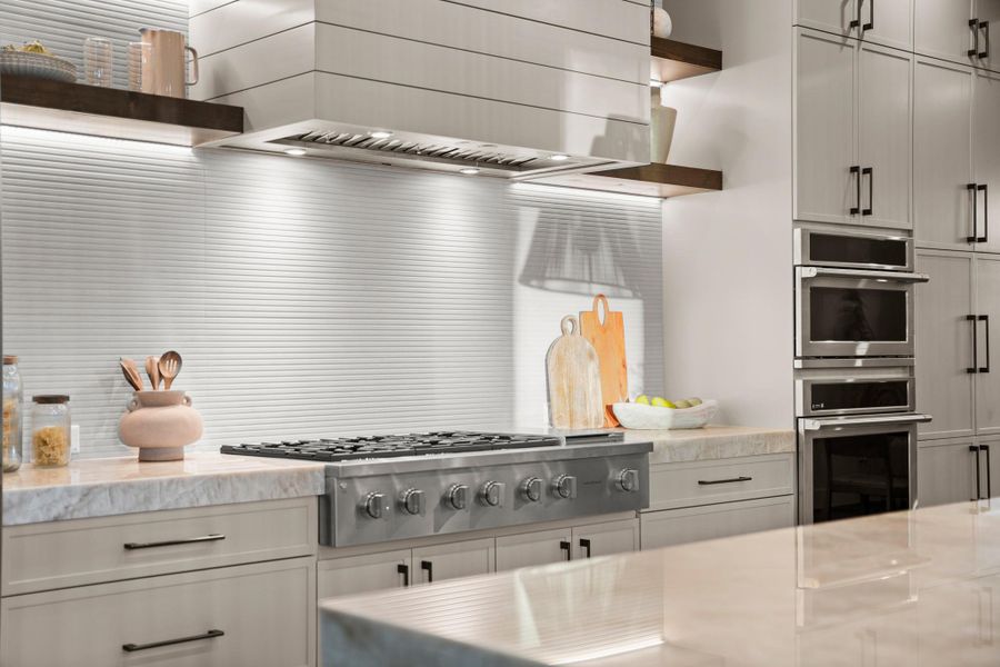 Kitchen featuring custom exhaust hood, light stone countertops, appliances with stainless steel finishes, white cabinetry, and open shelves