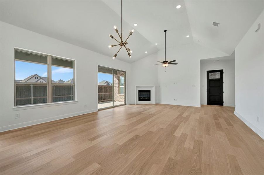 Unfurnished living room with a chandelier, a fireplace, light wood-type flooring, lofted ceiling, and ceiling fan Unfurnished living room with a chandelier, a fireplace, light wood-type flooring, lofted ceiling, and ceiling fan