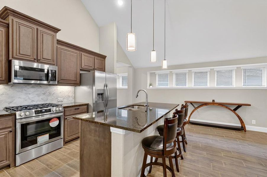 Kitchen featuring vaulted ceilings, wood-finish tile flooring, stainless steel appliances, a center island with bar seating, and ample cabinetry Kitchen featuring vaulted ceilings, wood-finish tile flooring, stainless steel appliances, a center island with bar seating, and ample cabinetry