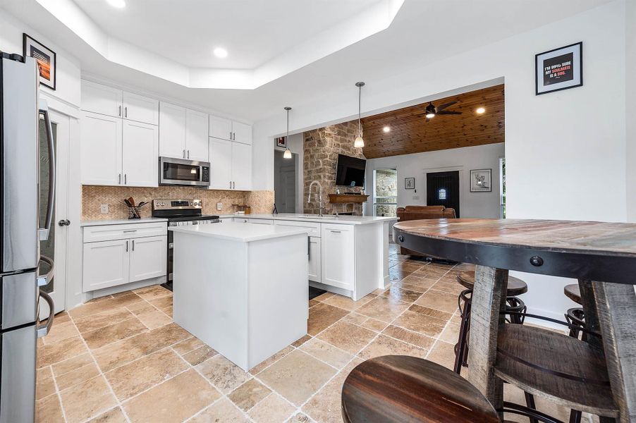The kitchen seamlessly connects to the main living area, featuring sleek white cabinetry, stainless steel appliances, and a spacious island that enhances both functionality and flow. The open design and warm wood accents create a comfortable and inviting atmosphere throughout the home.