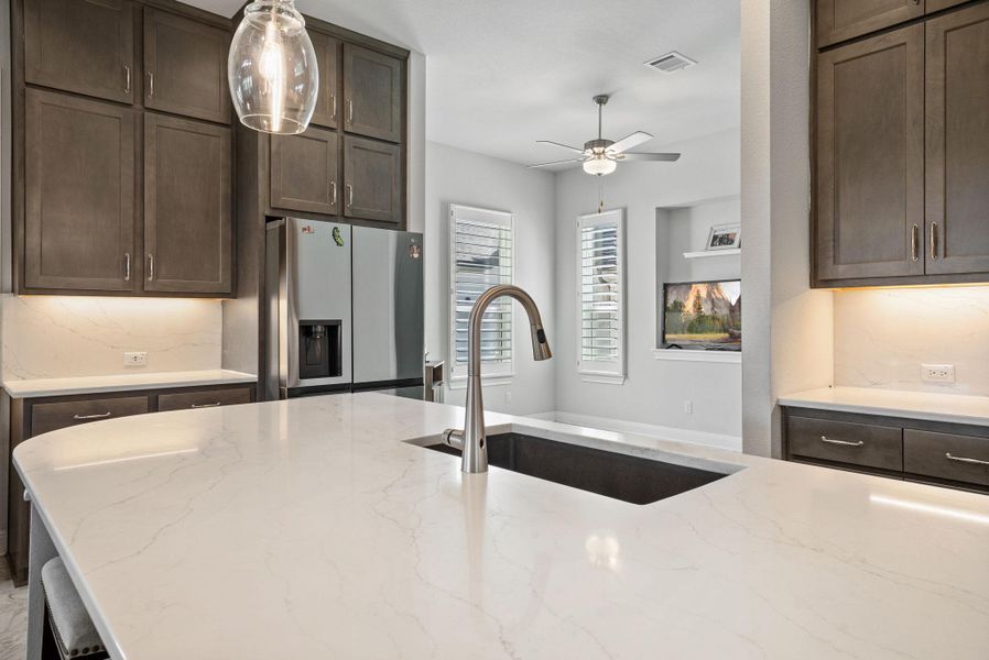 Kitchen with dark wood finish cabinets, backsplash, stainless steel refrigerator with ice dispenser, and light stone counters
