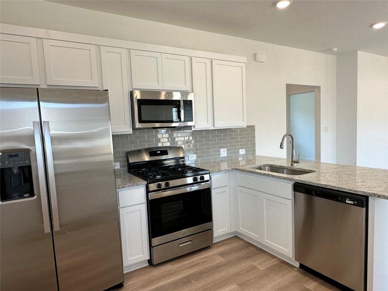 Kitchen featuring stainless steel appliances, white cabinetry, light stone countertops, backsplash, and light wood finished floors