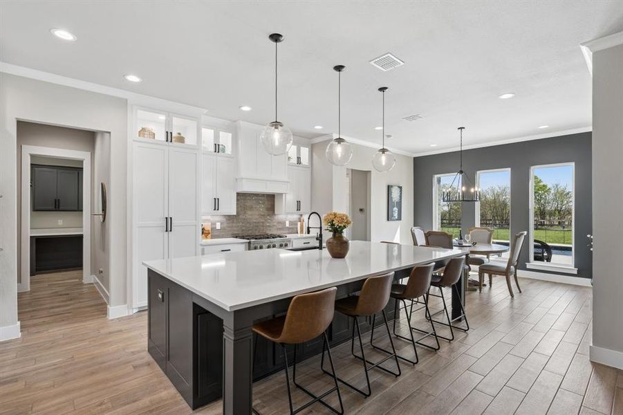 Dual tone kitchen with dual tone cabinetry, a large island with sink, glass fronted cabinets, a breakfast bar, and light wood-style flooring