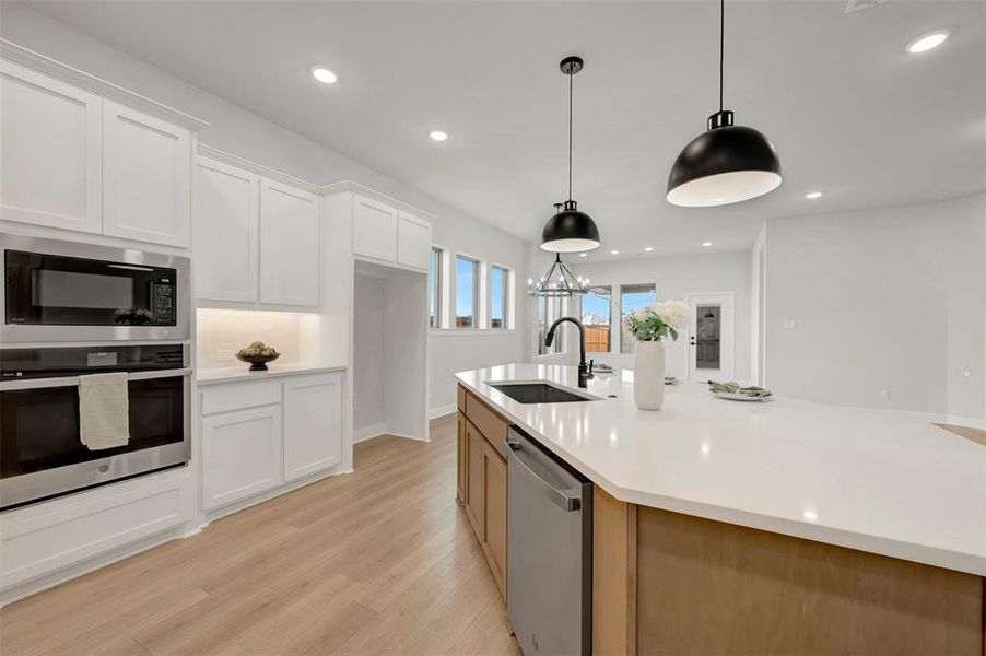 Dual tone kitchen with two tone cabinetry, stainless steel appliances, light wood finished floors, an island with sink, and light stone countertops
