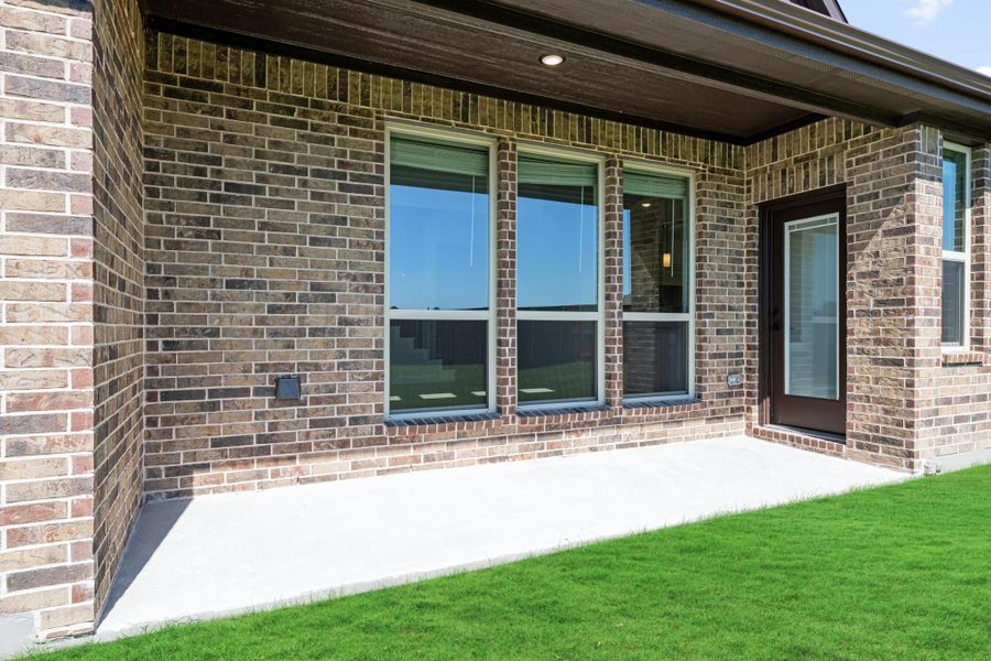 Brick home exterior with large windows, dark entry door, covered patio, and green lawn Brick home exterior with large windows, dark entry door, covered patio, and green lawn