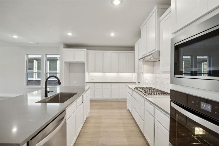 Kitchen with light wood-type flooring, tasteful backsplash, stainless steel appliances, sink, and white cabinets