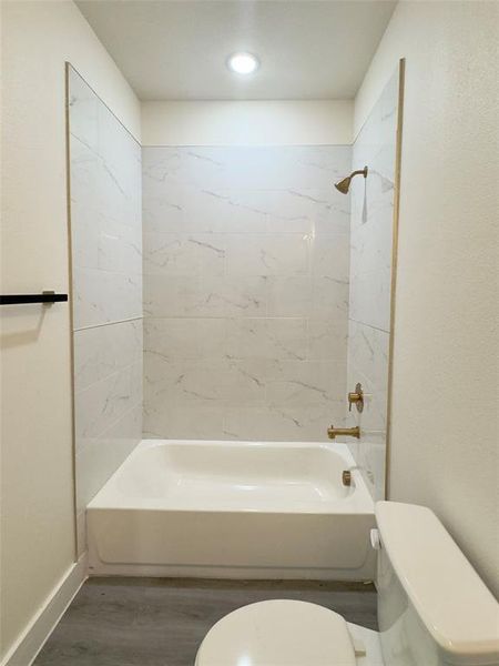 Bathroom featuring wood-type flooring, tiled shower / bath combo, and toilet