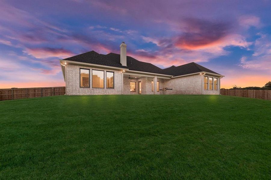 Back of property at dusk featuring brick siding, a chimney, and a fenced backyard Back of property at dusk featuring brick siding, a chimney, and a fenced backyard