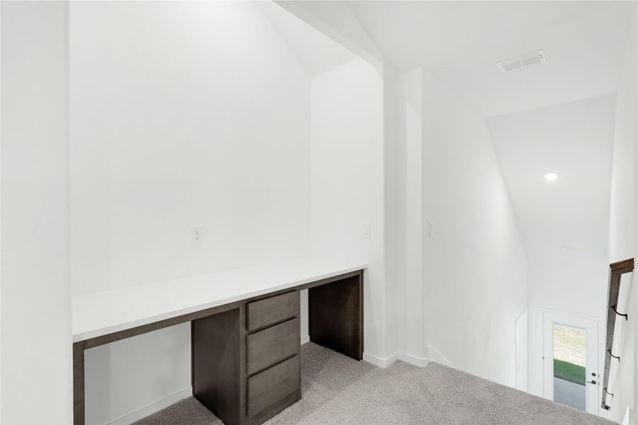 Built-in desk with dark wood drawers and white countertop in carpeted loft area with vaulted ceiling Built-in desk with dark wood drawers and white countertop in carpeted loft area with vaulted ceiling
